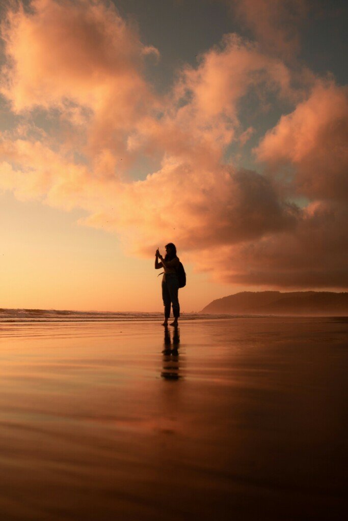 WOman on beach taking a picture of the sunset at the golden hour